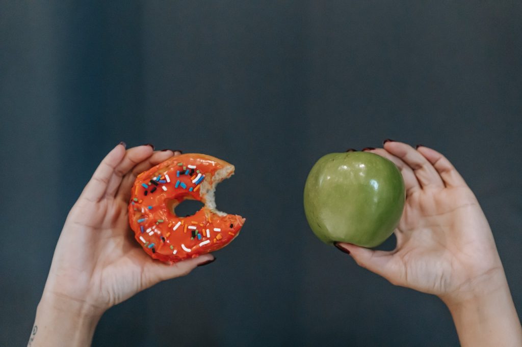 person holding a donut and an apple to show the pros and cons of snacking